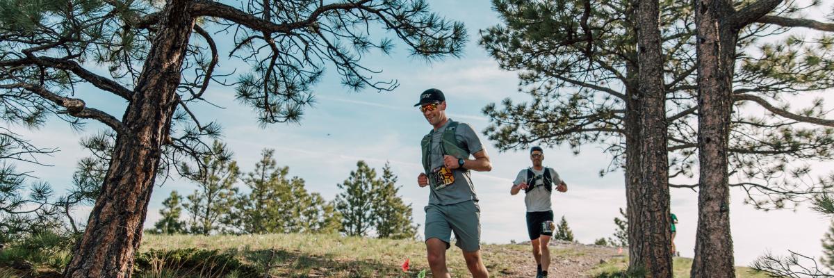 two men running through a Ponderosa pine forest on a hilltop