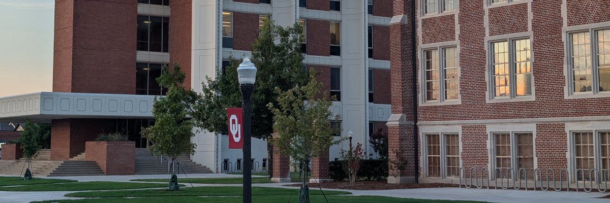 Engineering buildings at the University of Oklahoma, at sunset, with an OU banner visible on a streetlamp in the foreground.
