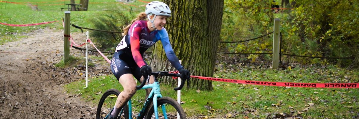 Photo by Ally Griffin on Unsplash - Photo of a woman with a white helmet riding a bike down a hill around a corner on a cyclocross course.