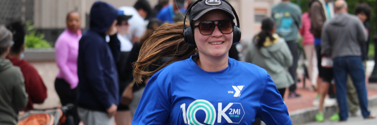 woman in a race shirt smiling as she cross the finish line with onlookers in background